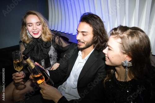 Happy glamorous girls with flutes of champagne and young man holding bottle