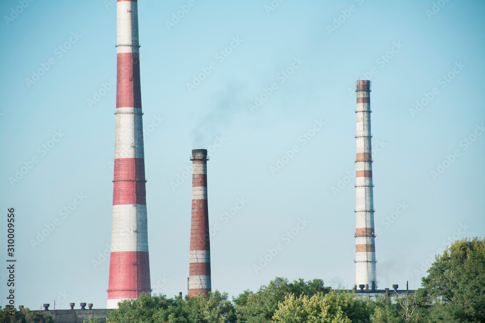 The pipes of the plant rise above the forest. Industrial landscape. Harmful environmental production. Environmental pollution. Smoke from the chimneys. Soot station.
