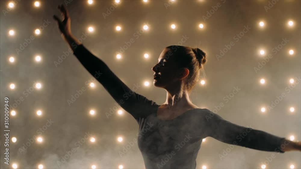 Silhouette of ballerina in black tutu is dancing ballet in the dark studio with smoke and the lights on the background. Silhouette of ballerina in black tutu is dancing ballet in the dark studio with smoke and the lights on the background.