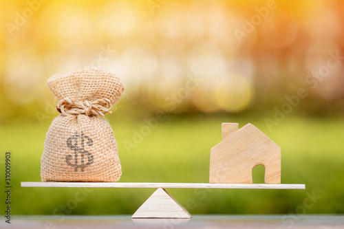 Home and money bag put on the scales with balance put on the wood in the public park, Saving for buy a new house or real estate and loan for plan business investment in the future concept.