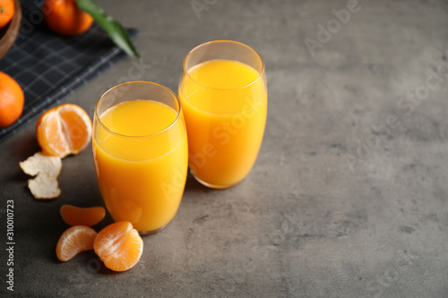 Fresh tangerines and glasses of juice on grey table. Space for text