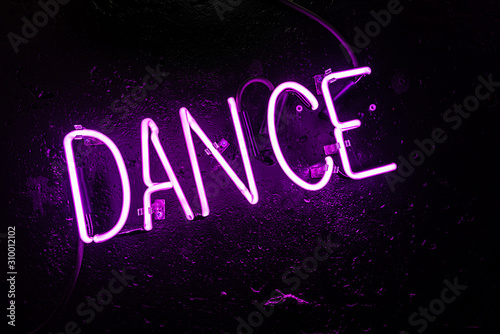 Purple neon light creating the word "DANCE" on a black wall in a disco or night club