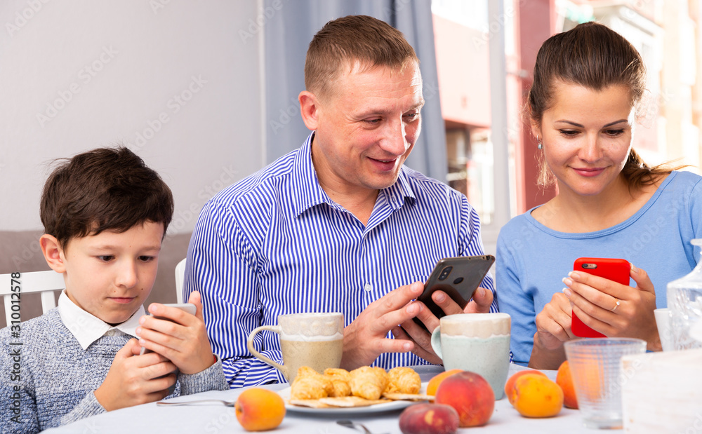 Parents and teen son using phones at kitchen