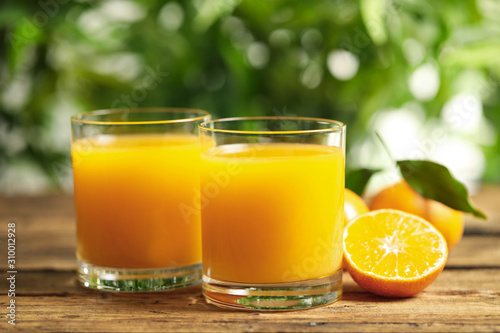 Glasses of fresh tangerine juice and fruits on wooden table