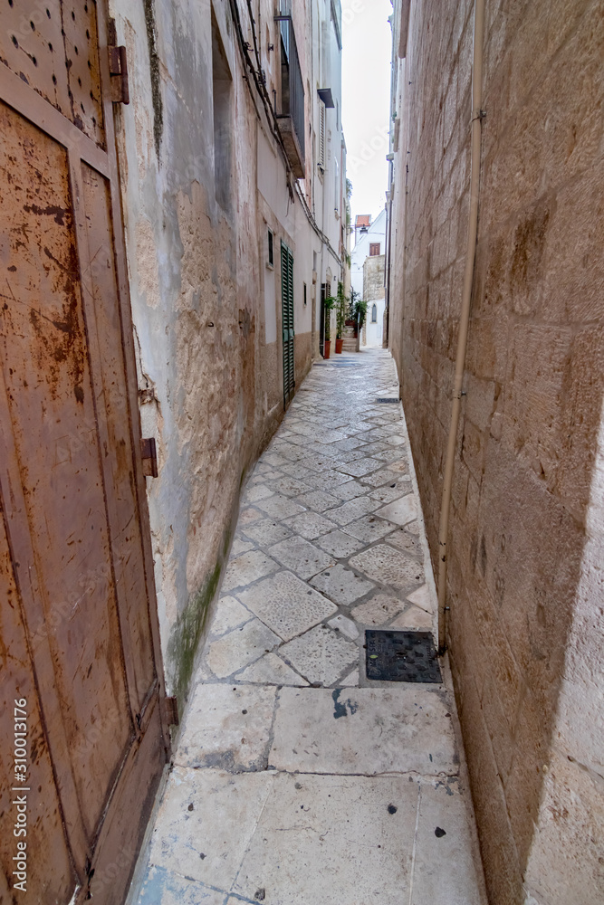Very narrow street with limestone patio view with old building walls from the old town, Noci. Puglia. Italy, sunny and warm summer day