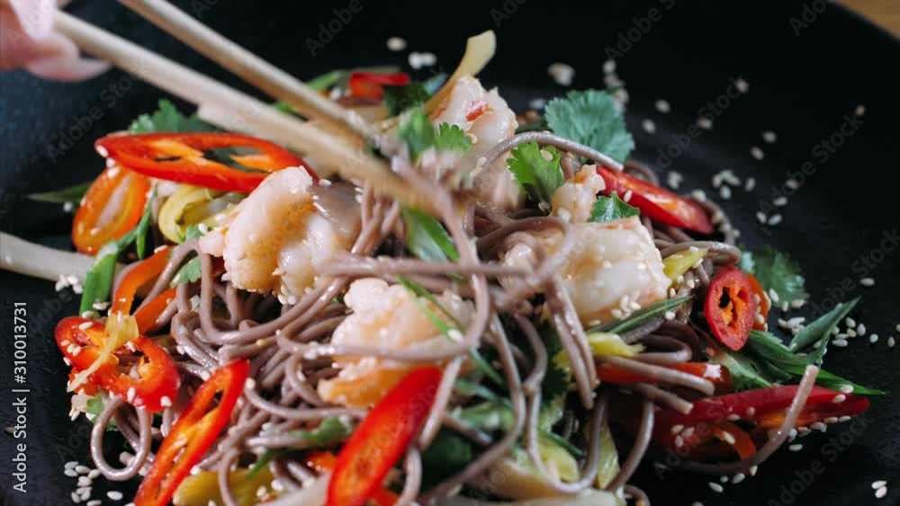 Close-up eating traditional asian soba stir-fry noodles with shrimp by chopsticks, top view. Asian food concept. Close-up eating traditional asian soba stir-fry noodles with shrimp by chopsticks, top view. Asian food concept.