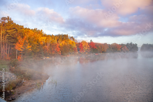Mist rises from the Oxtounge river during fall season early morning as sunlight reaches the colourful fall foliage