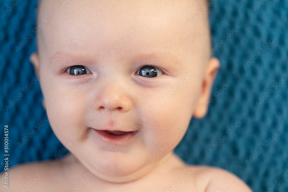 Close up of a happy smiling baby against a blue blanket background Close up of a happy smiling baby against a blue blanket background