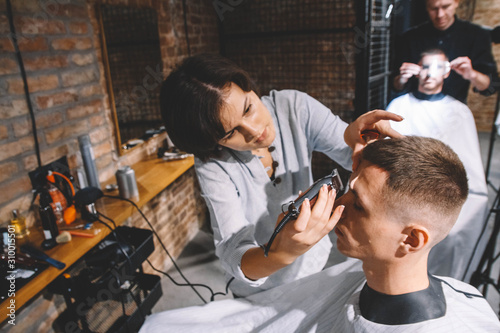 Beautiful woman hairdresser shaves the client's head with a electric trimmer in barber shop. Advertising and barber shop concept