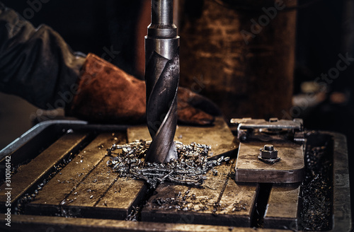 Drilling hole in the metal with giant drill at steel factory by worker male.