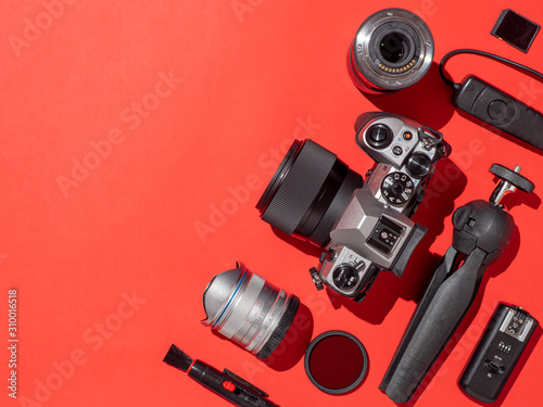 Photographer workplace with dslr camera, lens, pen tablet and camera accessories on red background. Camera, photography, visual content concept. Flat lay or top view. Copy space. Hard light.