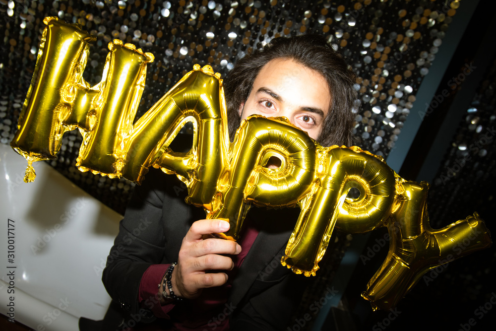 Young cheerful man holding golden inflatable balloon letters by his face