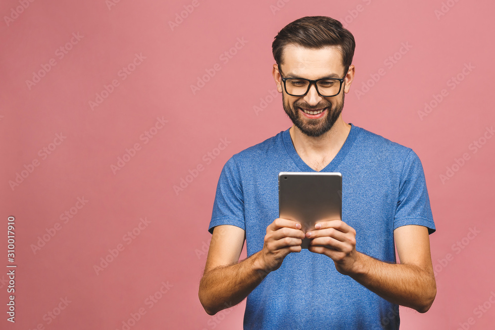 Happy young man in casual standing and using tablet isolated over pink background. Happy young man in casual standing and using tablet isolated over pink background.