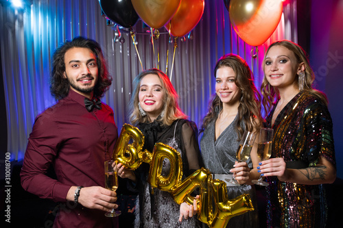 Three happy girls and young man holding flutes of champagne and balloons