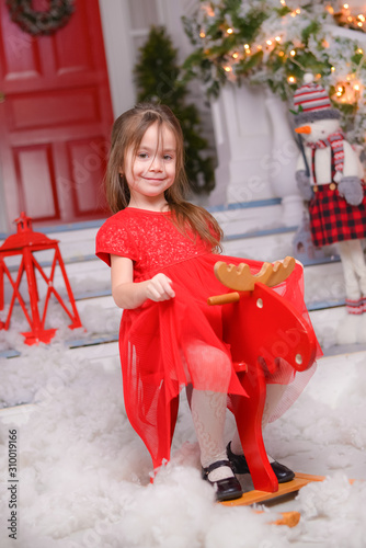 little beautiful girl in a red dress rides a wooden donkey, New Year's decor, Christmas mood