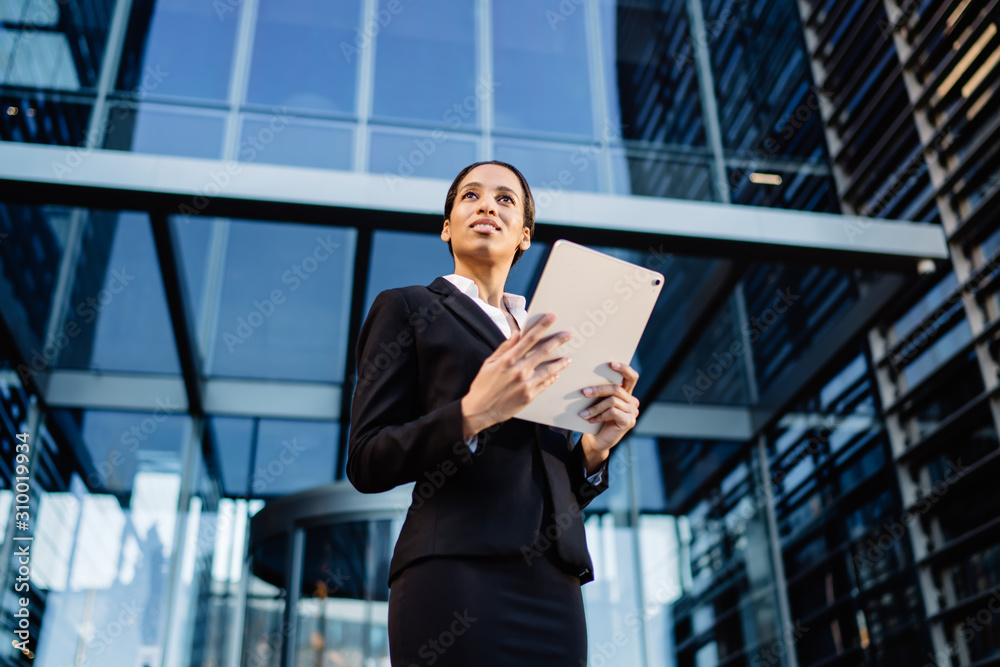Smiling black businesswoman with tablet on street
From below of confident and inspired ethnic woman in suit holding modern tablet and looking away on background of glass skyscraper Smiling black businesswoman with tablet on street
From below of confident and inspired ethnic woman in suit holding modern tablet and looking away on background of glass skyscraper