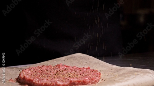 Cook makes meat medallions for burgers. Chef in black food gloves makes cutlet. Cutlets are leveled in steel ring in an even medallion. On top of pouring spices pepper and salt. photo