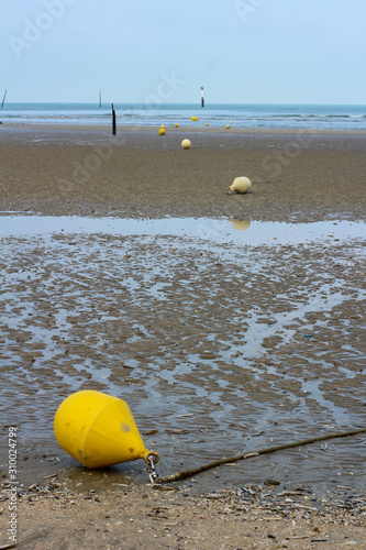 Empty beach with low tide and line of yellow buoys © Jenny