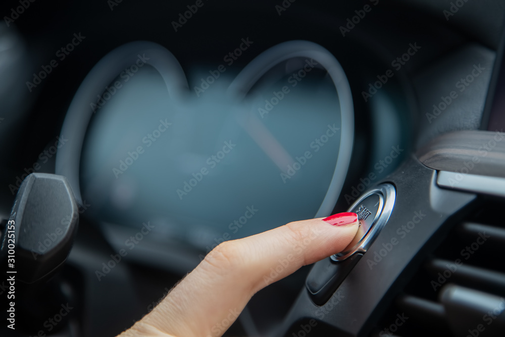 female finger presses the start stop engine button on a car dashboard. close-up, soft focus, in the background the dashboard and car speedometer in blur, side view