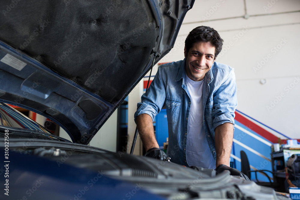 Cheerful man working in car workshop and fixing car engine with tool smiling at camera Cheerful man working in car workshop and fixing car engine with tool smiling at camera