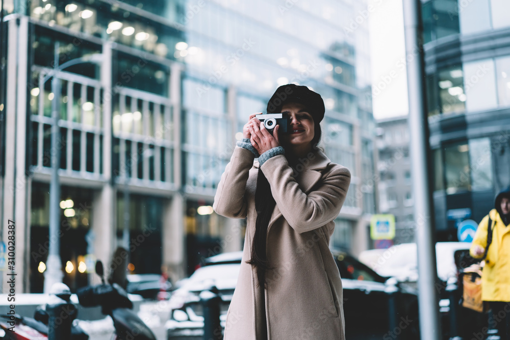 Young smiling lady in coat taking photo with camera