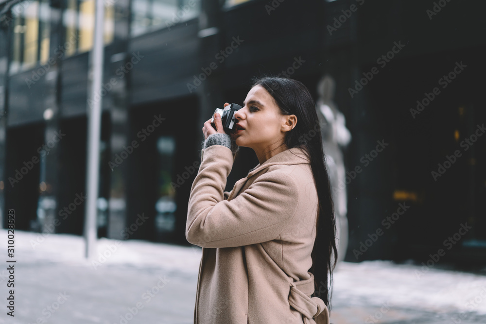 Young concentrated woman in coat taking photo with camera