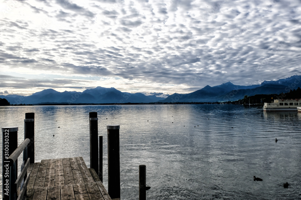 Cloudy landscape on Chiemsee lake. In the foreground are bridges for mooring boats. A mountain range is visible on the horizon. Bavaria, Germany