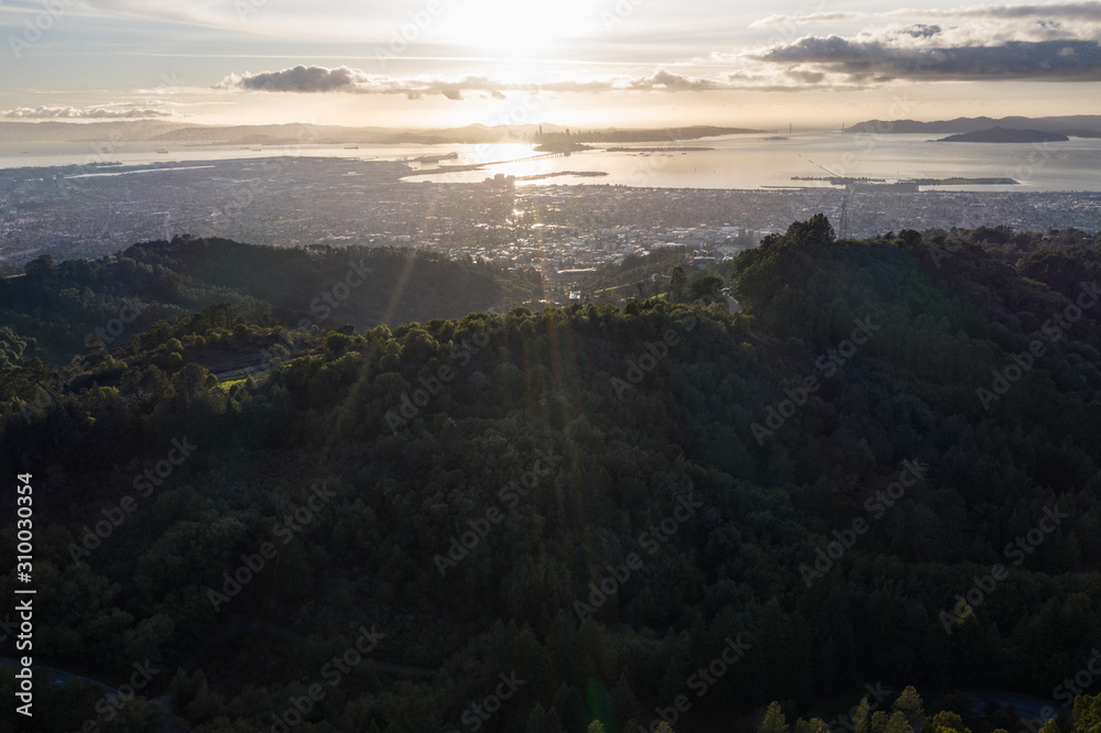 A serene sunset illuminates the densely populated San Francisco Bay area including Oakland, Berkeley, Emeryville, El Cerrito, and San Francisco in the distance.
