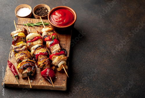 Meat skewers with grilled vegetables on a cutting board on a stone background with copy space for your text