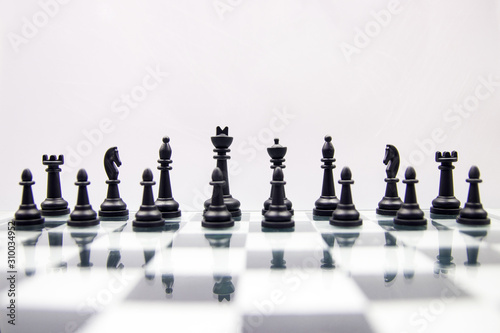 black chess pieces stand on a mirror chessboard on a white background