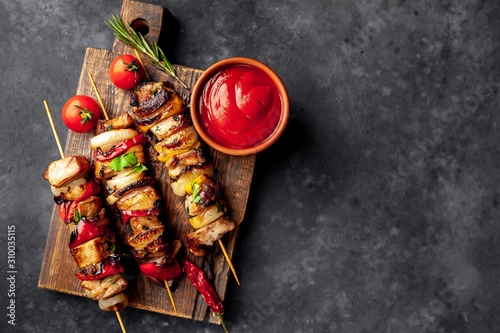 Meat skewers with grilled vegetables on a cutting board on a stone background with copy space for your text
