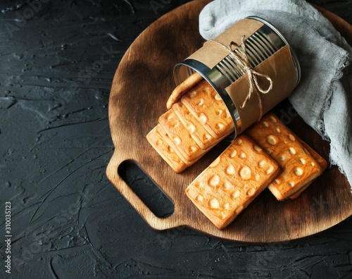 Cheese cookies in a tin on a wooden board on a dark background. Top view