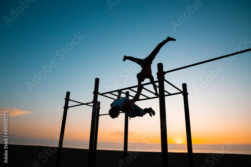 Two young men practicing calisthenics at an outdoor gym at sunrise
