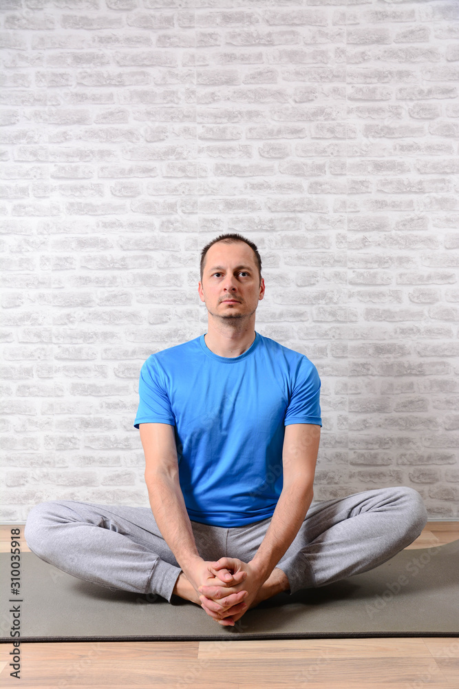 Fototapeta premium Peaceful attractive man practising yoga, meditating at home. Joyful man undergoing morning exercises. Vertical
