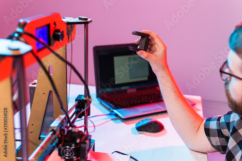 Technology and engineering concept - Male engineer working at night in the lab  he is adjusting a 3D printer components.
