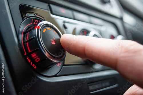 Button for heating the car seats close-up. The male hand presses the button for heating the seats of the car.