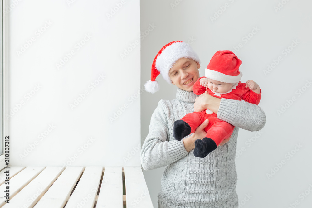 Obraz premium Fatherhood and holidays concept - Father with his baby boy wearing Santa hats celebrating Christmas