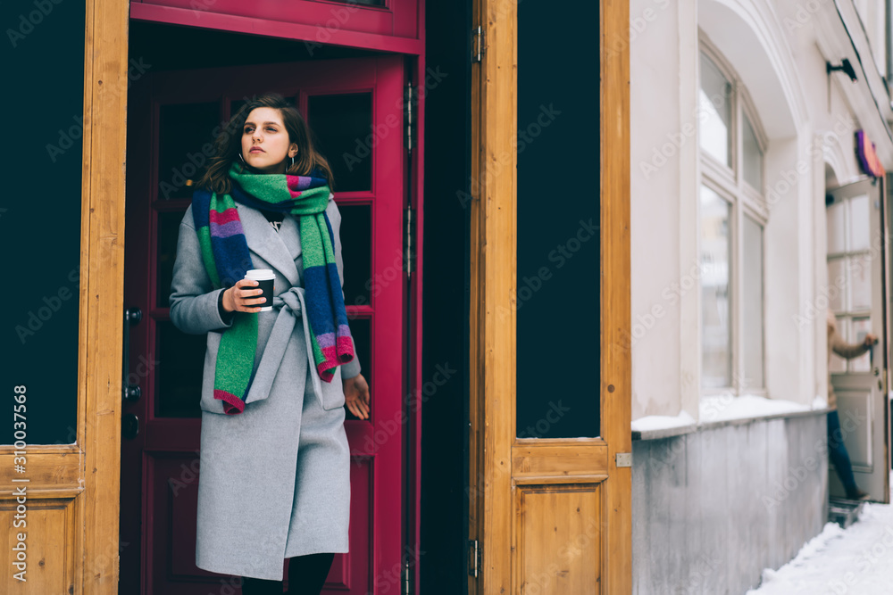 Fototapeta premium Young beautiful lady in winter outfit holding cup of coffee in front of cafe