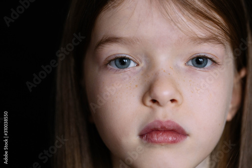close-up portrait of sad lonely little girl on black dark background. Girl face close up