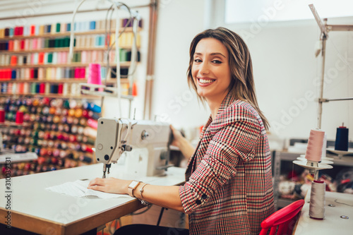 Portrait of happy dressmaker woman in studio. Background of colorful sewing thread.