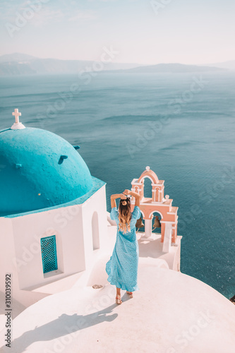 Young woman with blonde hair and blue dress in oia, santorini, greece with ocean view and churches