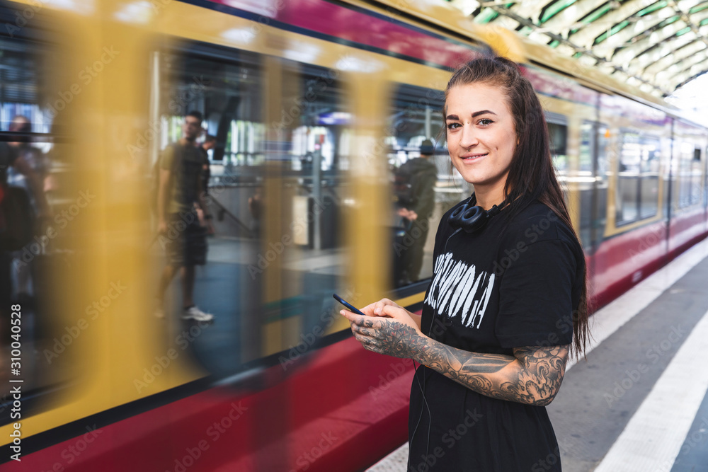 Portrait of tattooed young woman with smartphone and headphones standing on platform, Berlin, Germany Portrait of tattooed young woman with smartphone and headphones standing on platform, Berlin, Germany