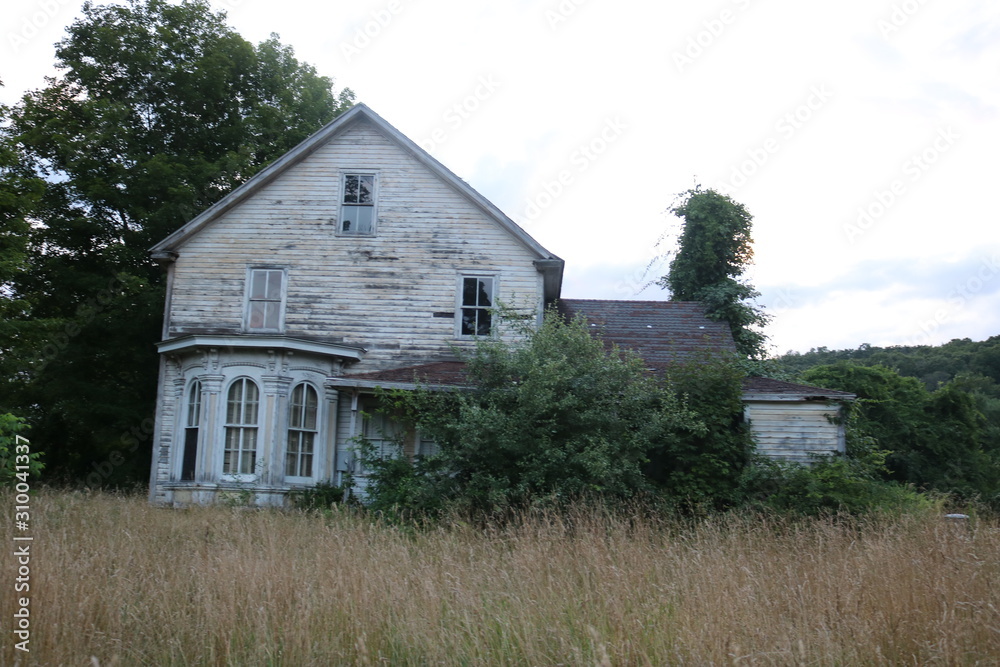 Old abandoned historic farmhouse with broken windows and peeling paint