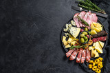 Typical italian antipasto with prosciutto, ham, cheese and olives. Black background. Top view. Space for text