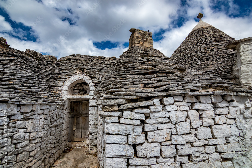 Roofs and entrance of truli, typical whitewashed cylindrical houses in Alberobello, Puglia, Italy with amazing blue sky with clouds, street view