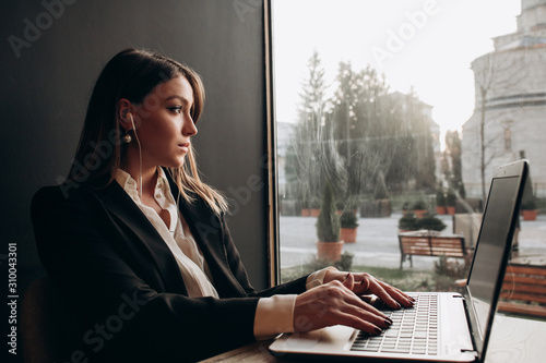 a beautiful girl wearning in office clothes with headphones sitting and working on the laptop in the cafe on the sun day photo