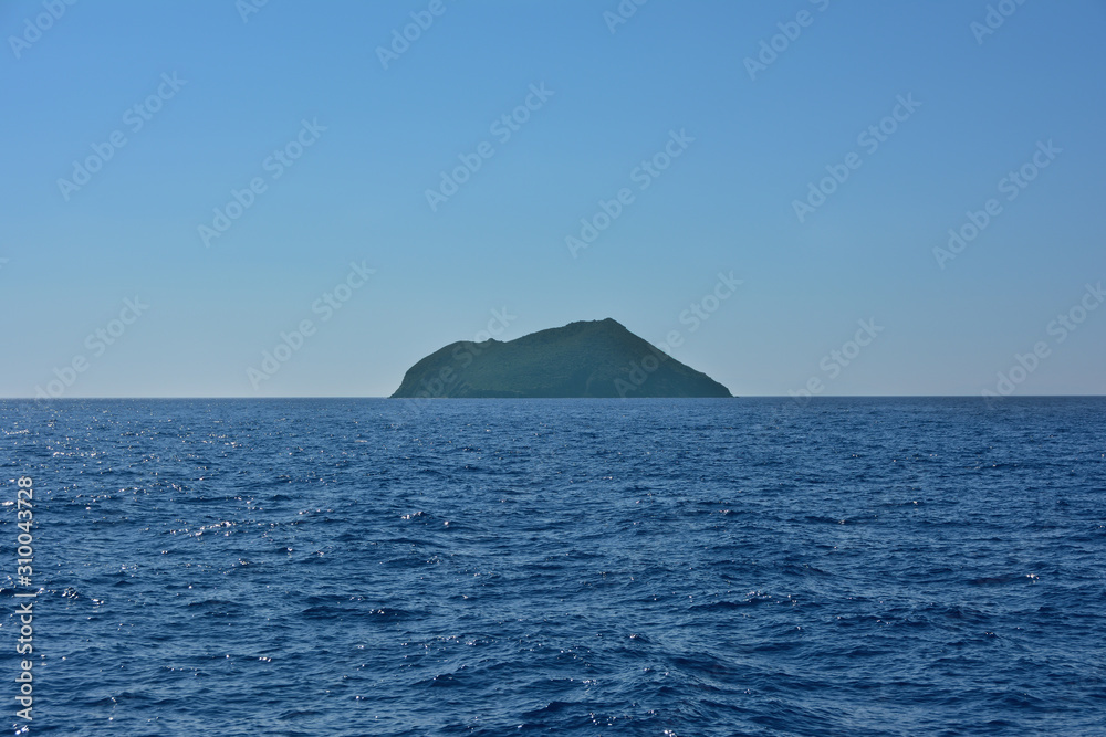 a large island on the horizon in the sea, on a bright cloudless summer day