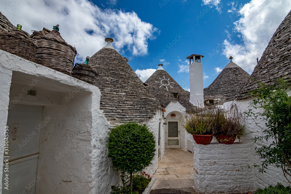 Roofs and entrances of truli, typical whitewashed cylindrical houses in Alberobello, Puglia, Italy with amazing blue sky with clouds, street view