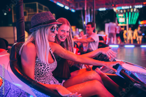 Girls having fun in electric bumper car in amusement park