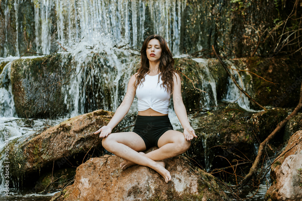 Young woman practicing yoga on a waterfall, sitting on rock Young woman practicing yoga on a waterfall, sitting on rock
